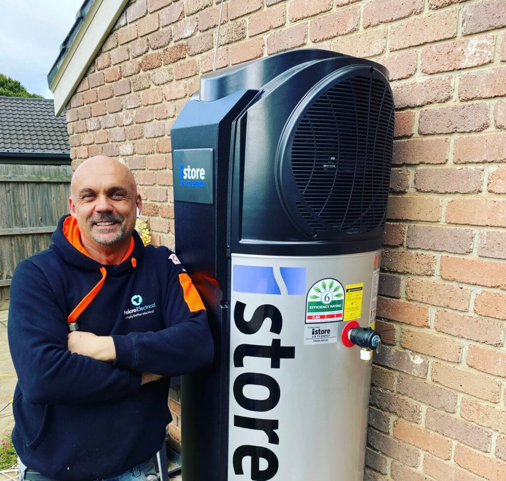 Electrician beside an iStore heat pump hot water unit on a brick wall